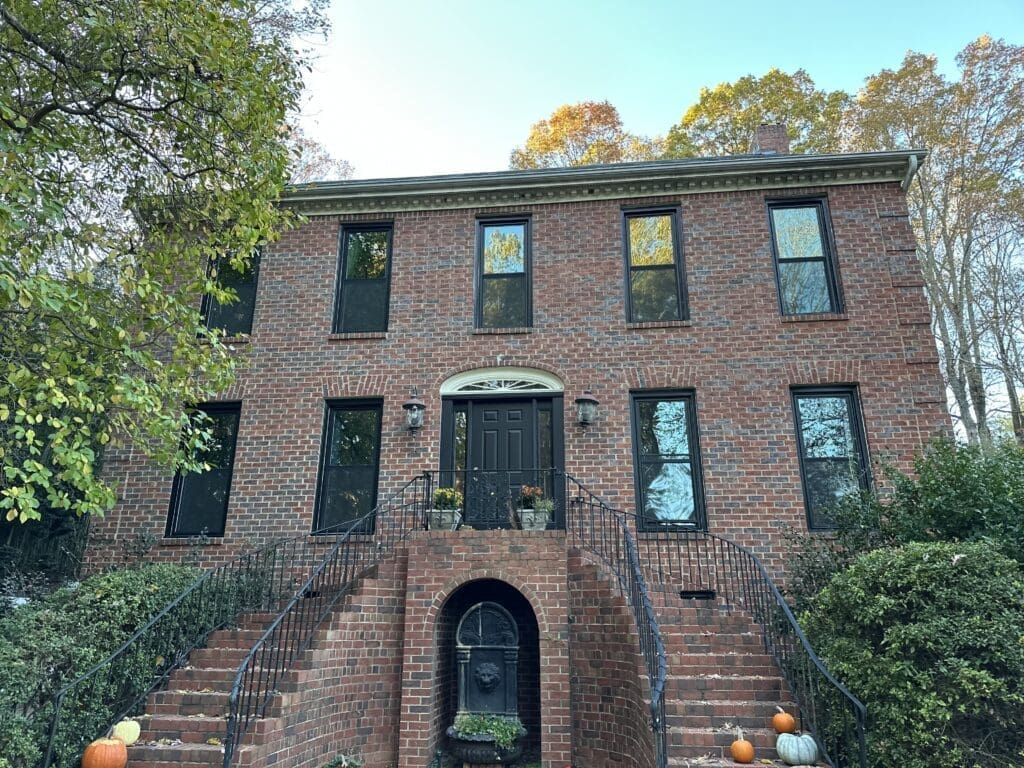 Red brick house with black-framed windows and double staircase, surrounded by greenery, near downtown Atlanta, Georgia.