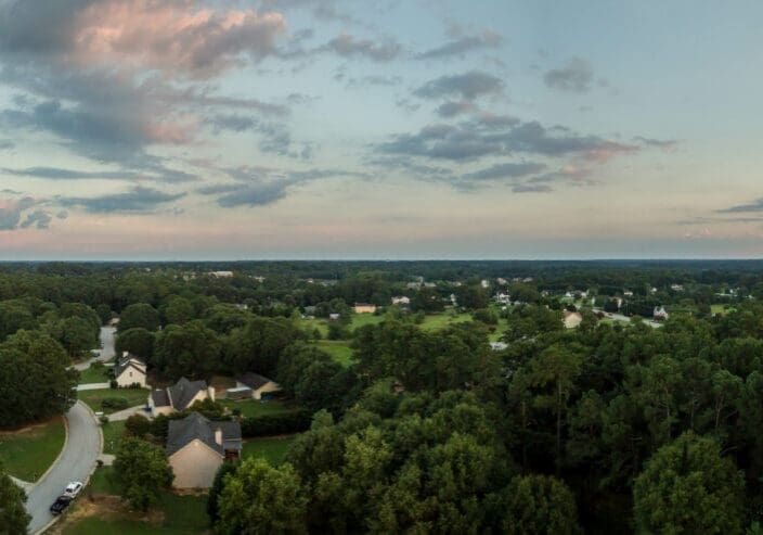 Panoramic aerial view of Loganville, Georgia, showing tree-lined suburban neighborhoods and sunset sky with scattered clouds.