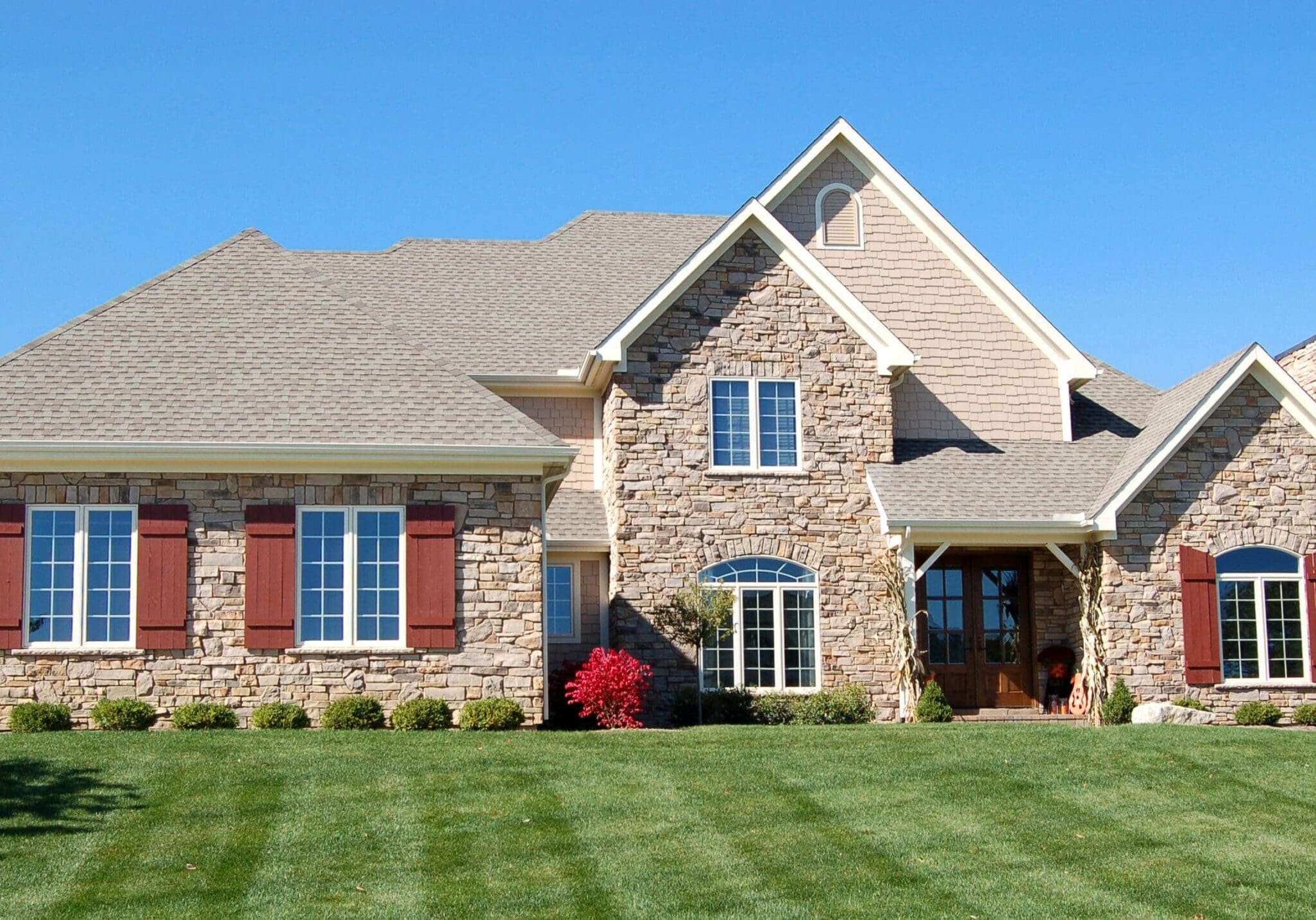 Stone-clad house with large windows and red shutters on manicured lawn in Alpharetta, Georgia, under a clear blue sky.