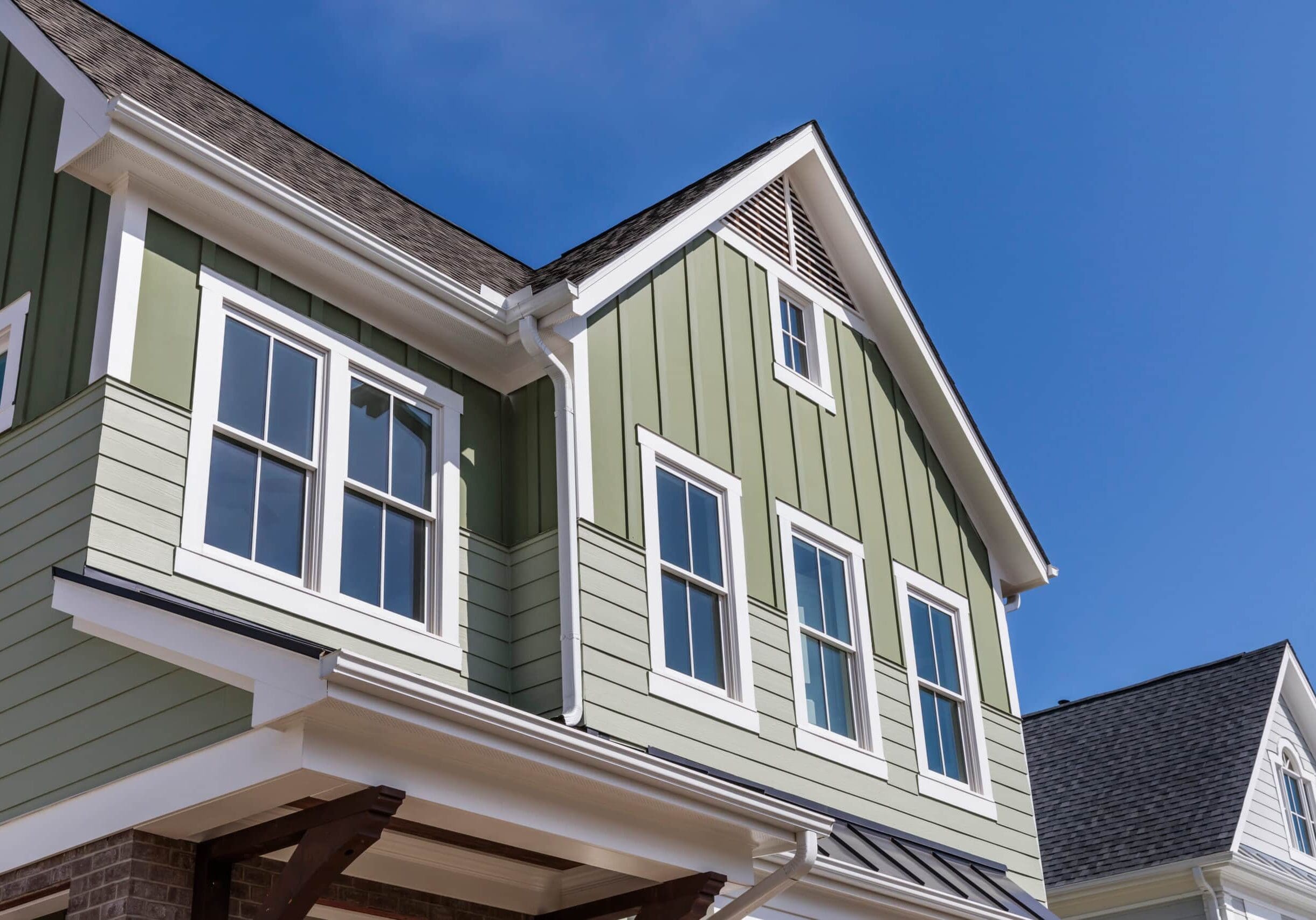 Green board and batten house with white-trimmed windows in Grayson, Georgia, under a clear blue sky.