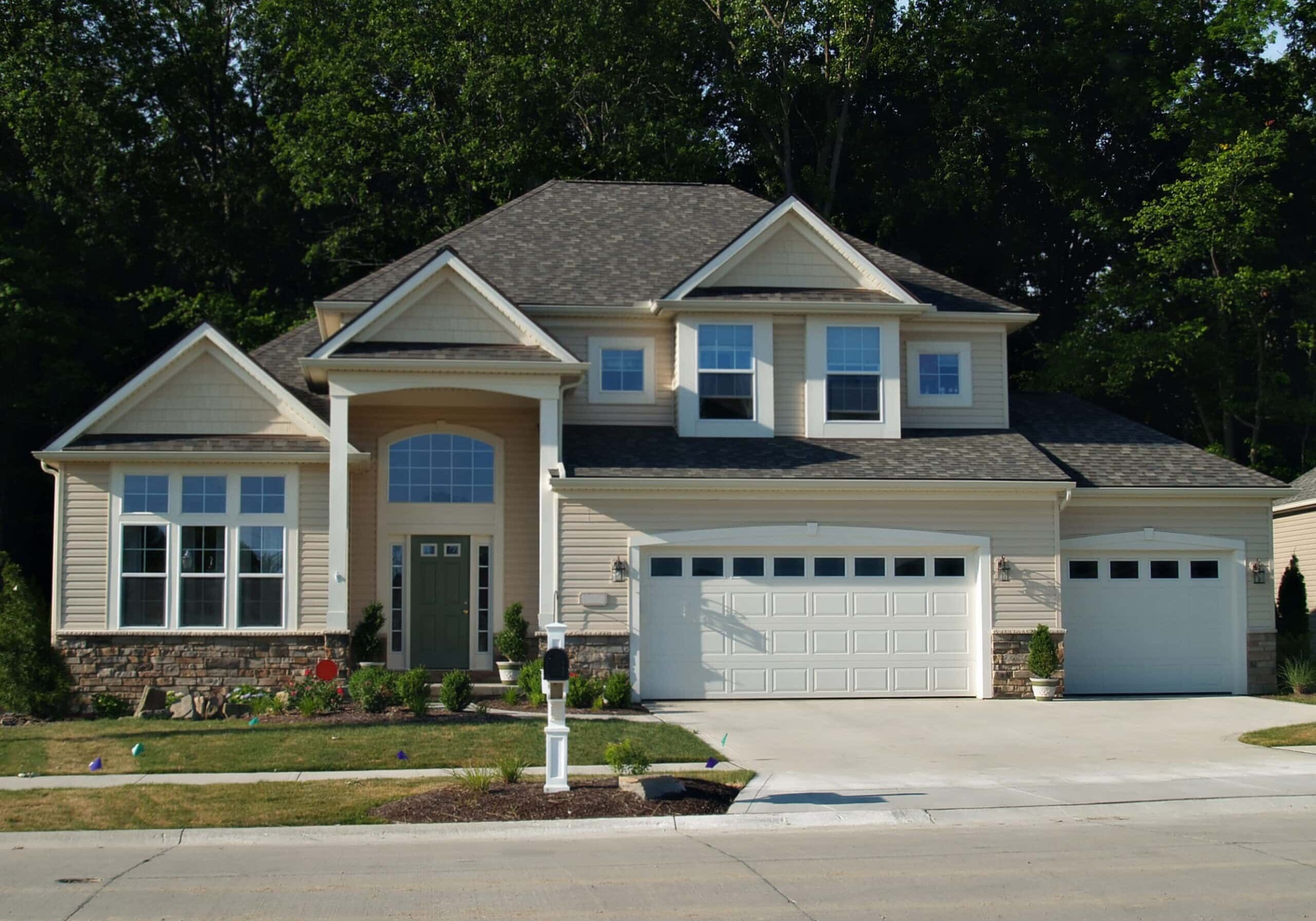Contemporary beige house with multiple large windows and three-car garage in John’s Creek, Georgia, on a sunny day.