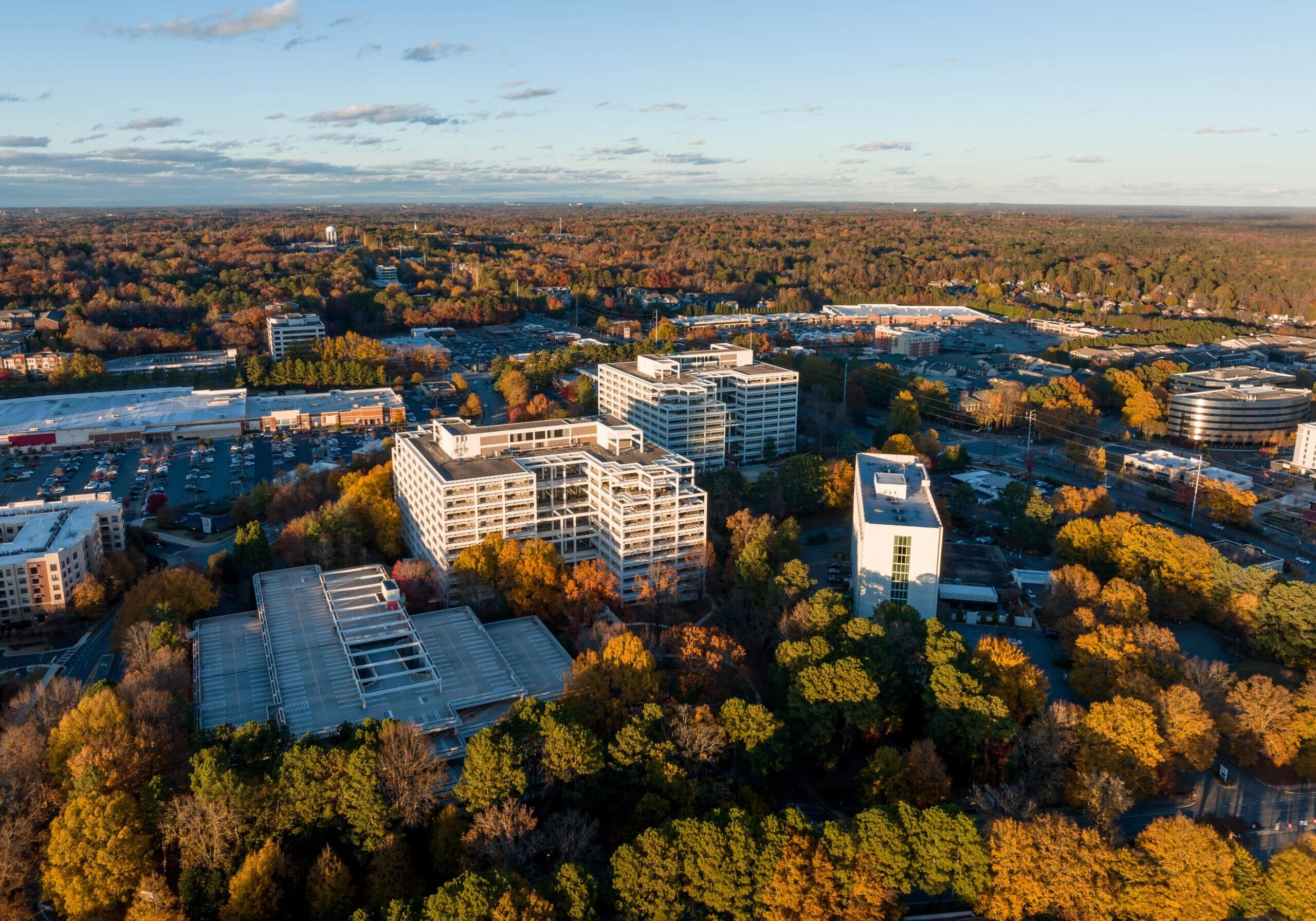 Aerial view of office buildings and shopping centers surrounded by autumn trees in Marietta, Georgia, under a clear sky.