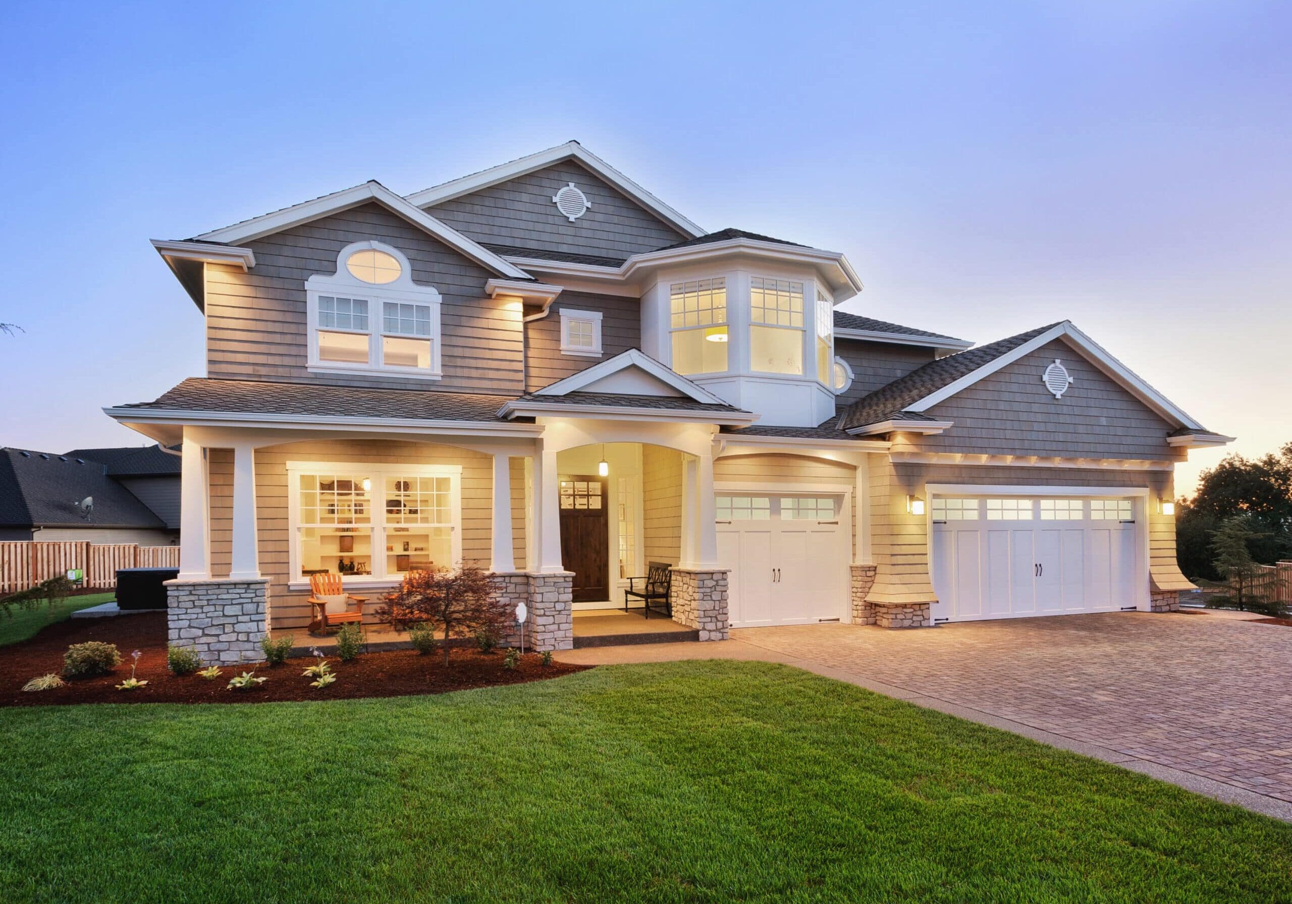 Contemporary two-story home with gray siding, large grid windows, and three-car garage in John’s Creek, Georgia at dusk.