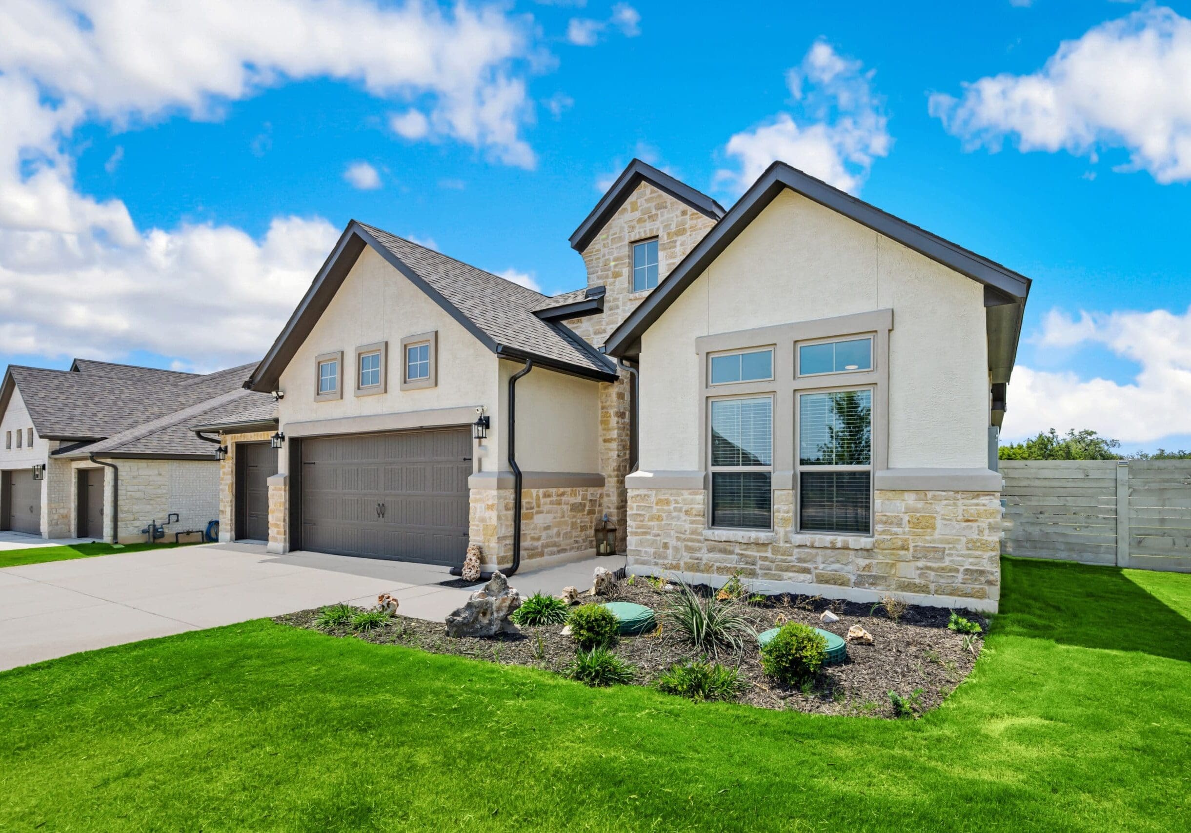 Modern stone and stucco home with double garage and large windows in Grayson, Georgia, set against a bright blue sky.