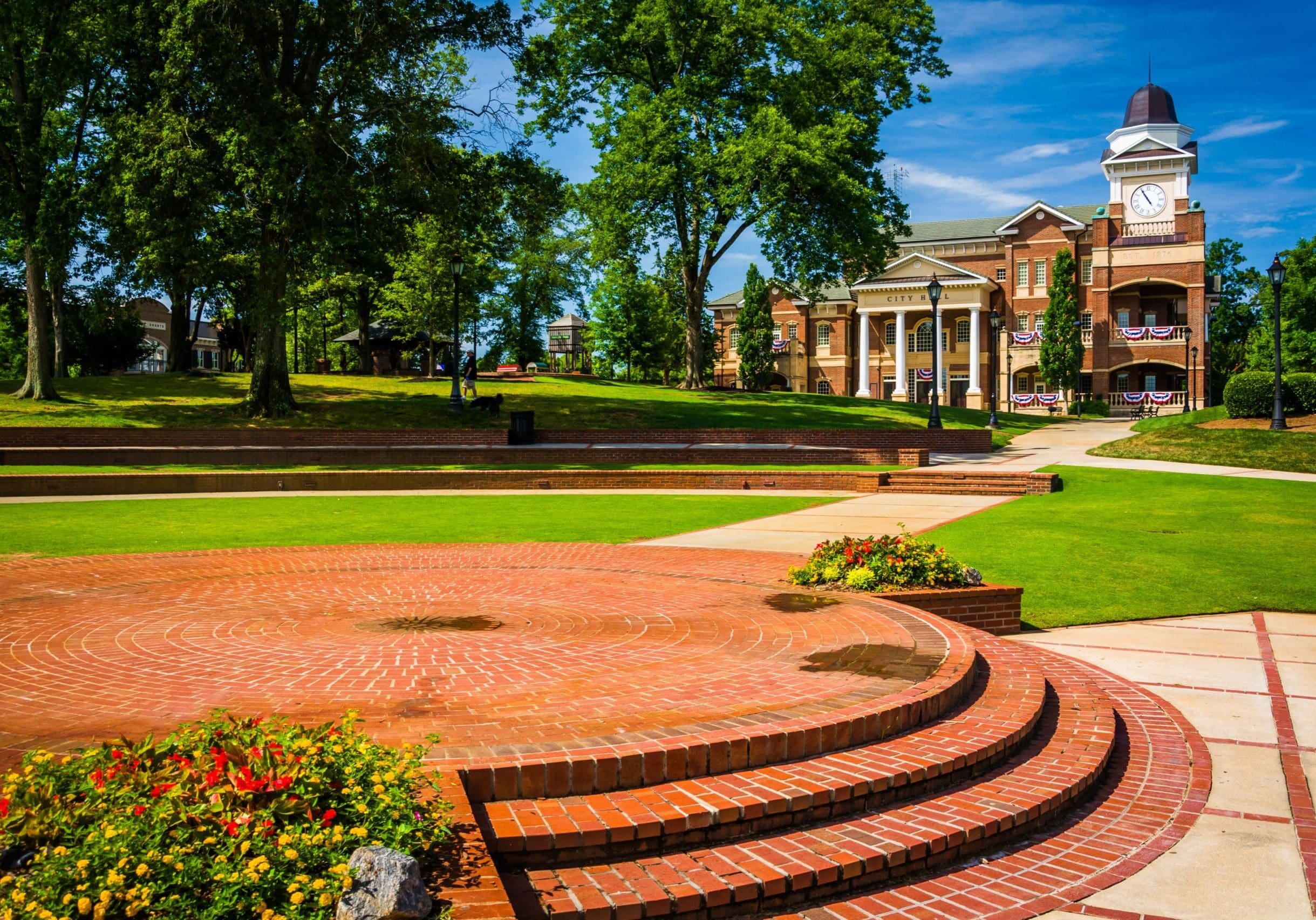 City hall with tall windows and clock tower in Duluth, Georgia, surrounded by green lawns, brick amphitheater, and trees.